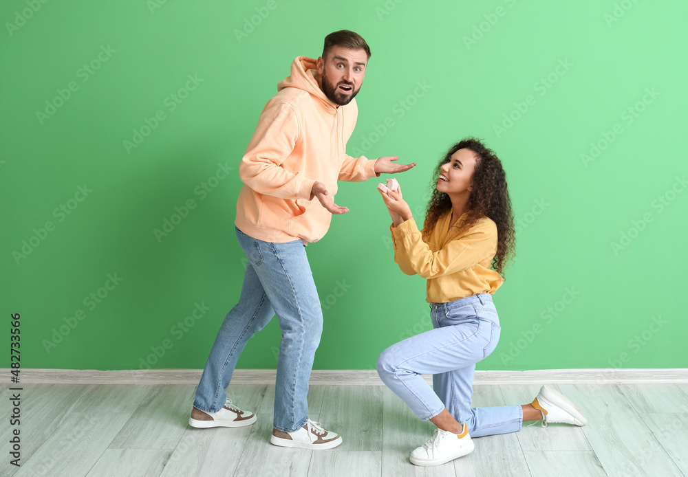 Young woman proposing to her shocked boyfriend on color background Young woman proposing to her shocked boyfriend on color background