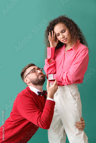 Young man proposing to his thoughtful girlfriend on color background