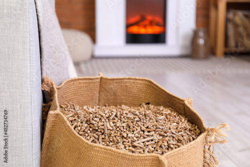 Bag with wood pellets near sofa in living room, closeup photo