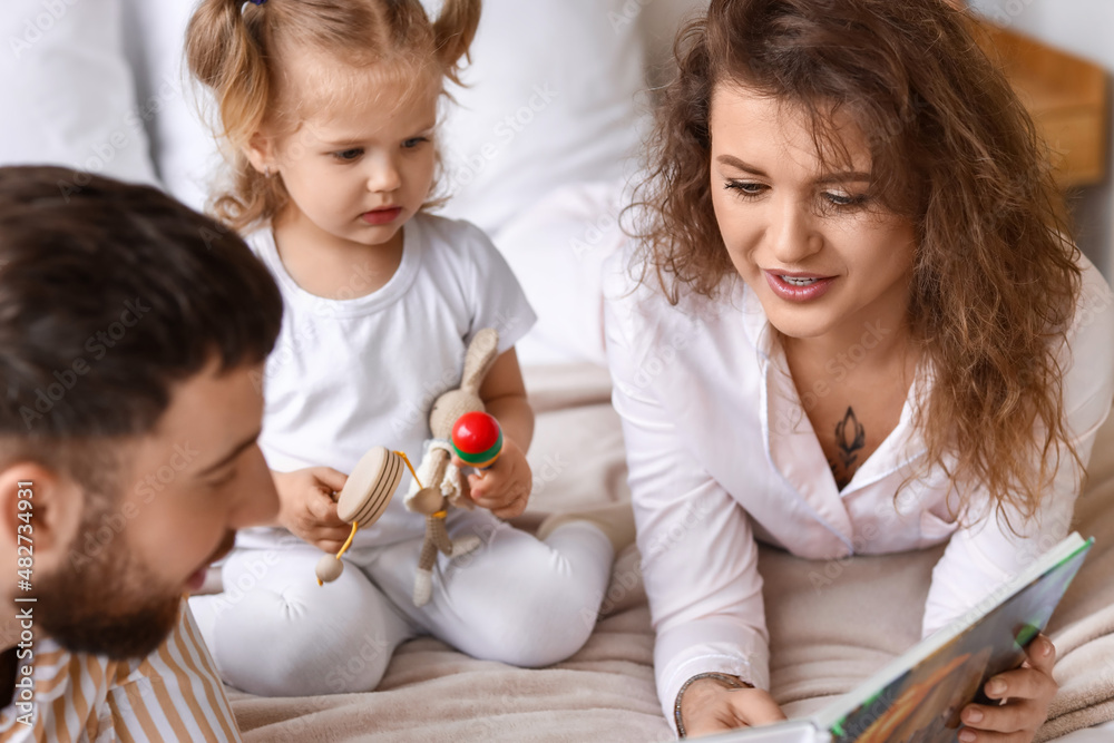 Happy young family reading book in bedroom at home Happy young family reading book in bedroom at home