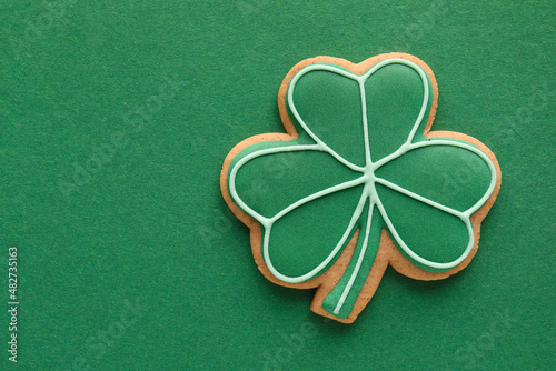 Tasty gingerbread cookie in shape of clover leaf for St. Patrick's Day celebration on green background photo