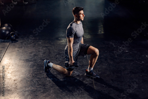 A strong sportsman doing lunges with dumbbells in his hands in a gym. photo