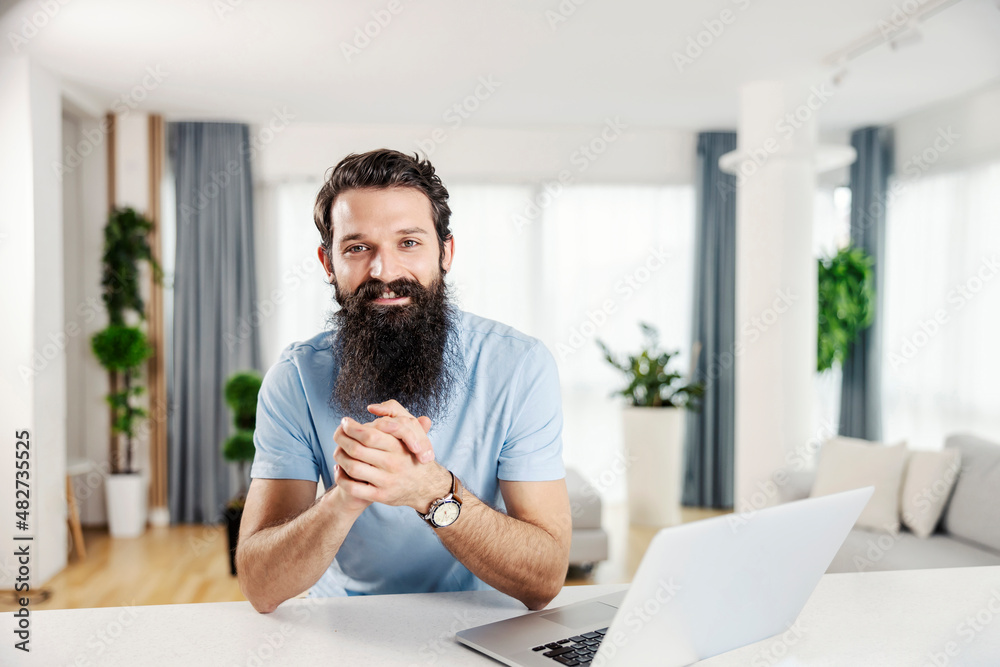 A smiling bearded man at his cozy home looking at the camera.