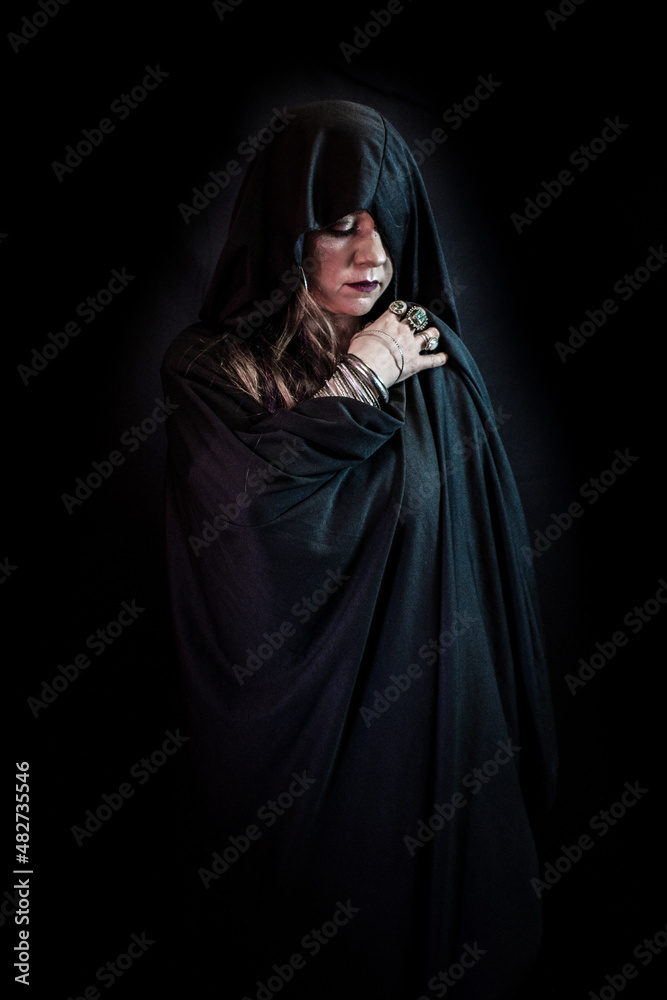 Hechicera con capa negra en las sombras mirando hacia abajo Hechicera con capa negra en las sombras mirando hacia abajo