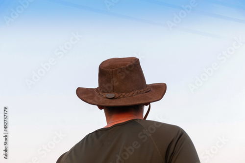 Back view of a young shirtless man wearing a cowboy hat. Young cowboy looking on blue sky away. Adventure western concept