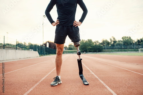A handicapped runner standing on running track at stadium with hands on hips.