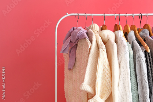 Rack with stylish warm sweaters near pink wall