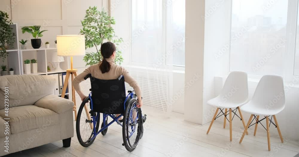 Woman in wheelchair looking out through window at home Woman in wheelchair looking out through window at home