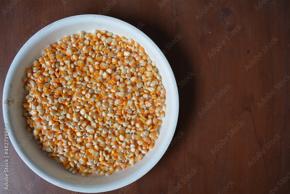 Orange corn kernels on a white tray, on a brown wooden texture background Orange corn kernels on a white tray, on a brown wooden texture background