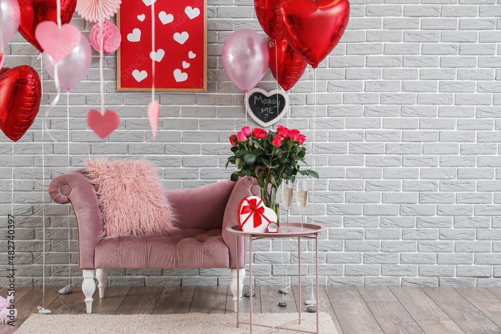 Obraz premium Interior of room with armchair and table with flowers, glasses of champagne, engagement ring and gift box near grey brick wall