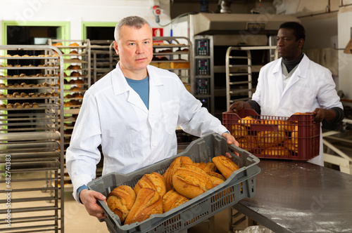 Two experienced bakers arranging fresh baked bread in small bakery