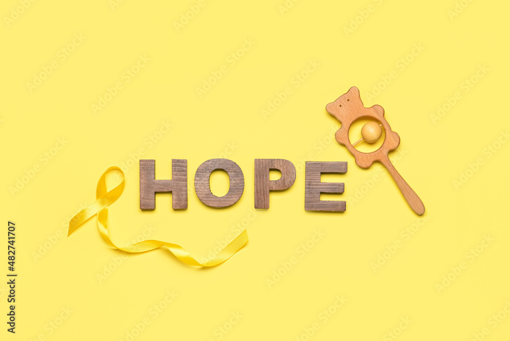 Golden awareness ribbon, rattle and word HOPE on yellow background. International Childhood Cancer Day