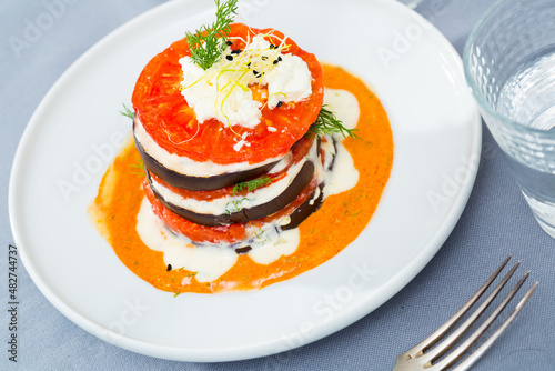 Grilled eggplant and tomatoes stack seasoned with spicy cream-tomato sauce served on white plate