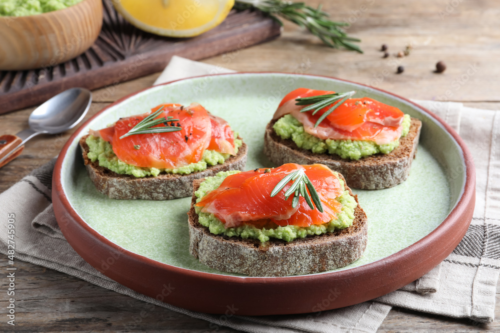 Delicious sandwiches with salmon, avocado and rosemary on wooden table Delicious sandwiches with salmon, avocado and rosemary on wooden table