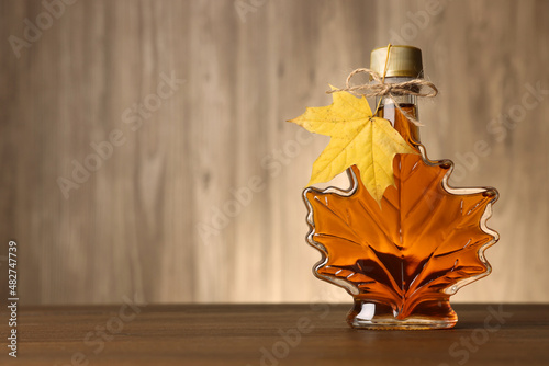 Fotografía Leaf shaped bottle of tasty maple syrup on wooden table
