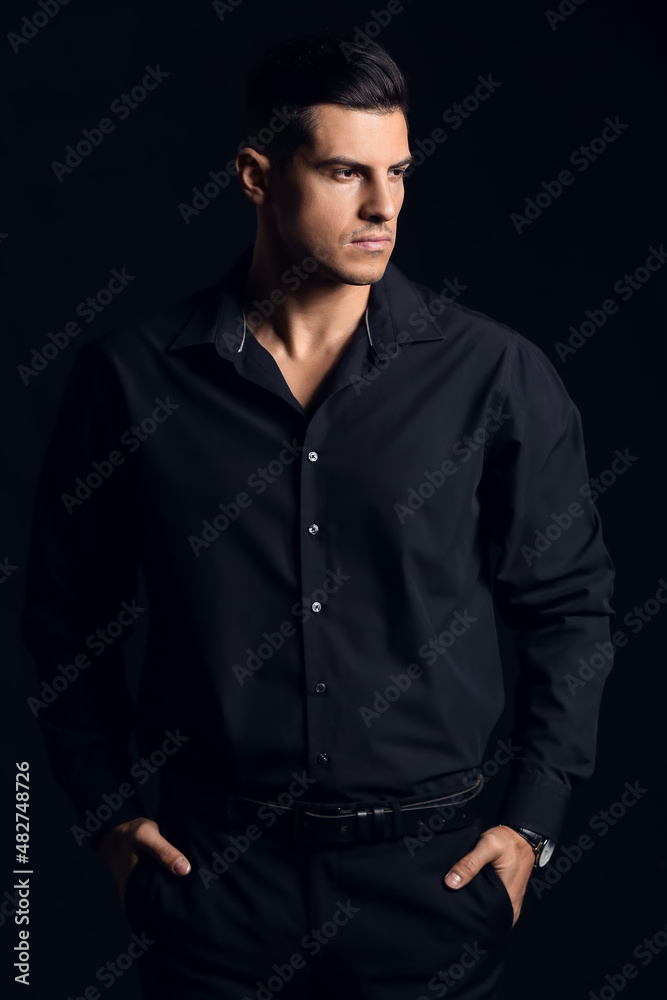 Fashionable gentleman keeping hands in pockets and looking aside on dark background