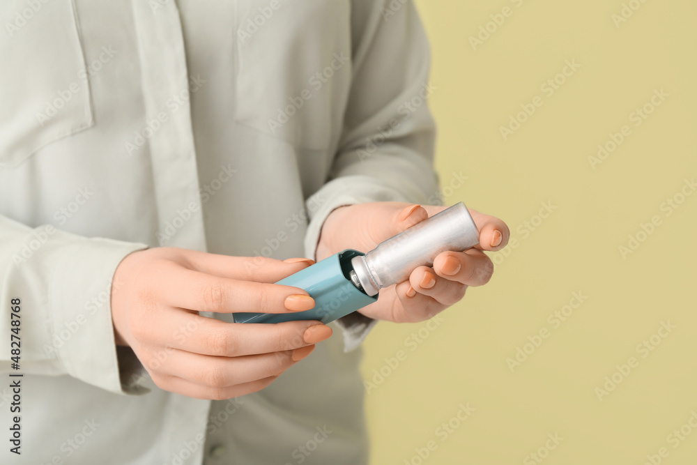 Woman holding asthma inhaler on beige background