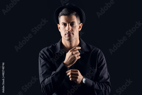 Fashionable gentleman in stylish hat adjusting sleeve on dark background