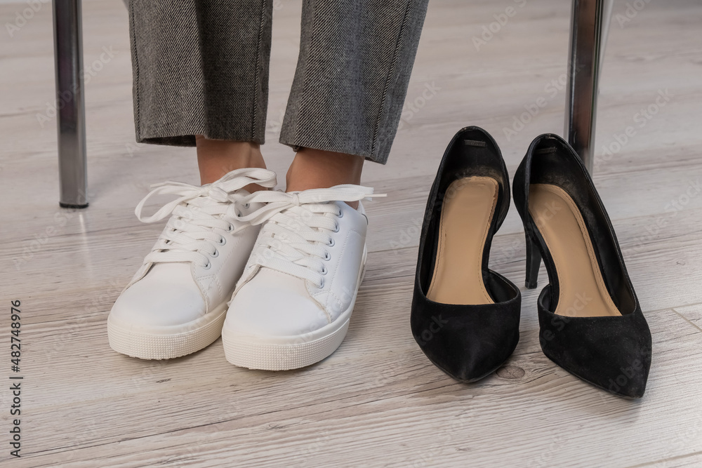 Close-up business woman takes off her shoes puts on white leather sneakers. Close-up business woman takes off her shoes puts on white leather sneakers.