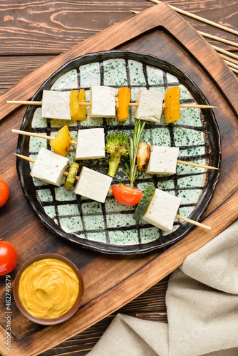 Board with grilled tofu cheese skewers and mustard on wooden background