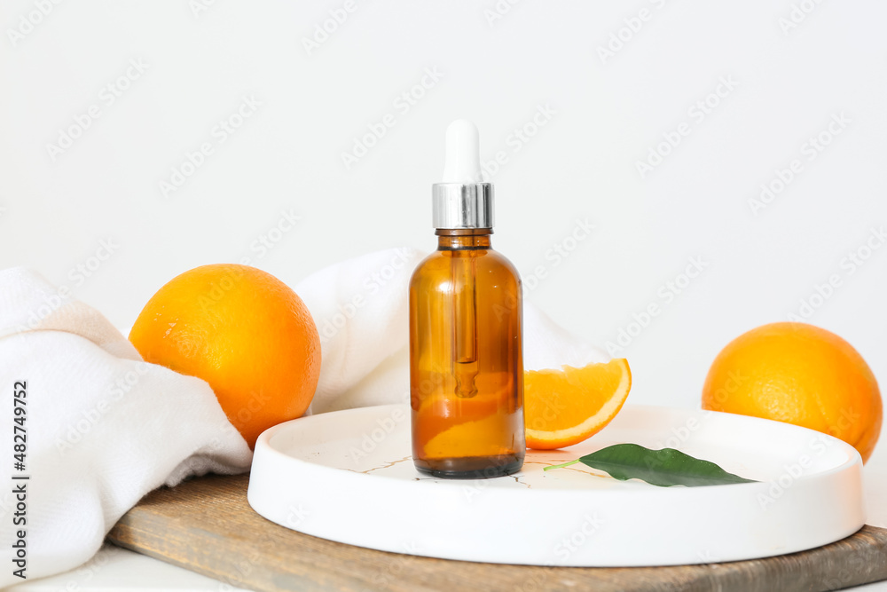 Bottle of essential oil and fresh oranges on light background