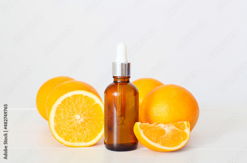 Bottle of essential oil and fresh oranges on light wooden table Bottle of essential oil and fresh oranges on light wooden table