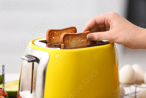 Woman taking bread slice from yellow toaster in kitchen, closeup