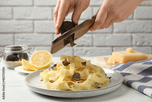 Woman slicing truffle over delicious pasta at white table, closeup