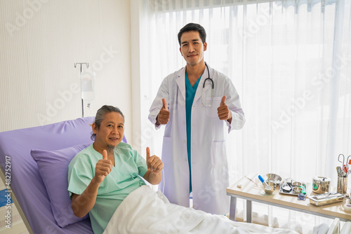 Elderly patient man with saline and doctor with stethoscope show thumbs up and happy to looking to camera. Doctor or nurse take care of senior patient health admission at hospital