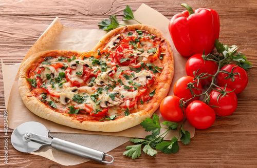 Tasty heart-shaped pizza and vegetables on wooden background. Valentine's Day celebration