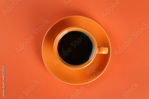 Coffee in cup on orange background, top view