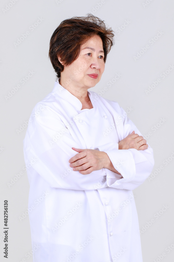 Elegant senior woman as professional chef confidently standing with arm crossed and wooden spoon and fork in restaurant kitchen Elegant senior woman as professional chef confidently standing with arm crossed and wooden spoon and fork in restaurant kitchen