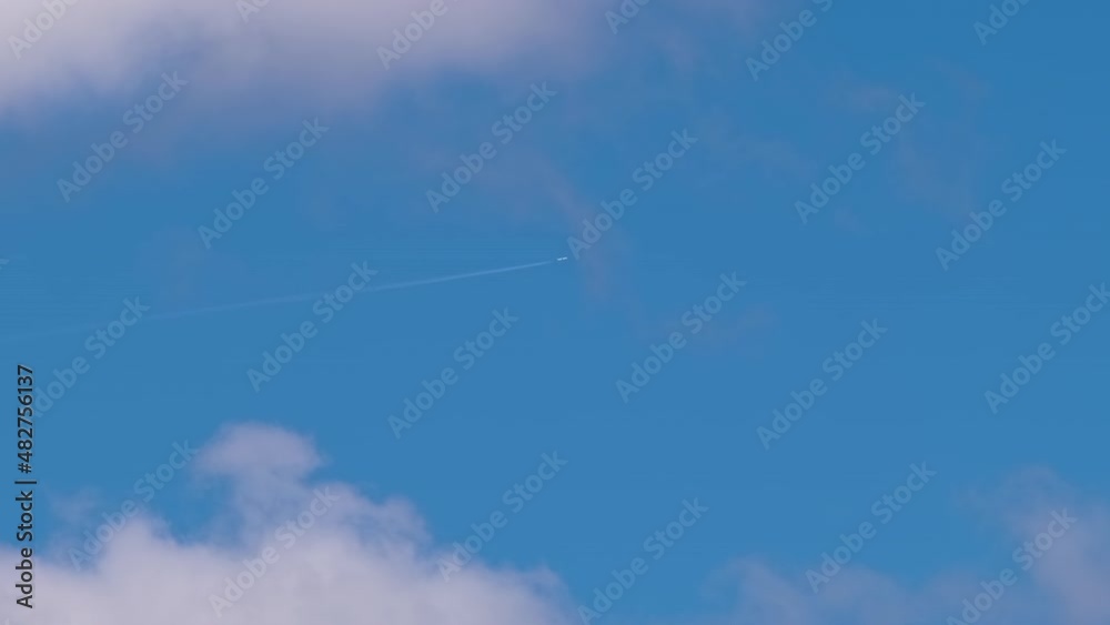 Distant passenger jet plane flying on high altitude on blue sky with white clouds leaving smoke trace of contrail behind. Air traveling concept Distant passenger jet plane flying on high altitude on blue sky with white clouds leaving smoke trace of contrail behind. Air traveling concept