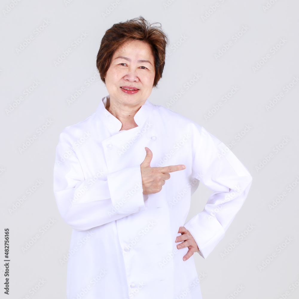 Elegant senior woman as professional chef confidently standing with arm crossed and wooden spoon and fork in restaurant kitchen