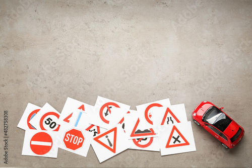 Many different road sign cards and toy car on grey table, flat lay with space for text. Driving school