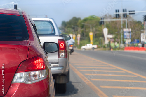 Traffic conditions on roads in Thailand. Red car parked at the end of a traffic light on an asphalt road. Turn on brake light. Traffic conditions during the clear daytime in the provinces. © thongchainak