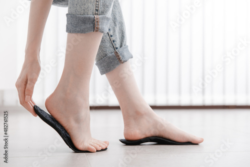 Woman fitting orthopedic insole indoors, close up. Girl holding an insole next to foot at home. Orthopedic insoles. Foot care banner. Flat Feet Correction. Treatment and prevention of foot diseases. © Maksim
