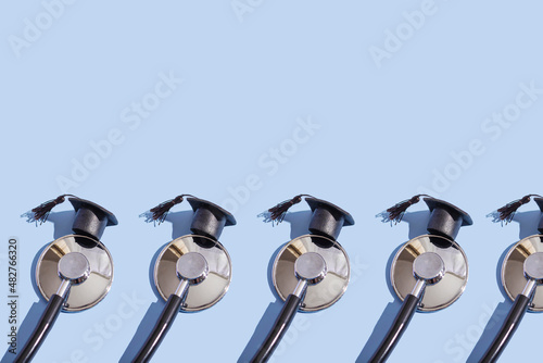 Stethoscope and graduation cap with hard shadow on blue background. Medical education concept, closeup with copy space