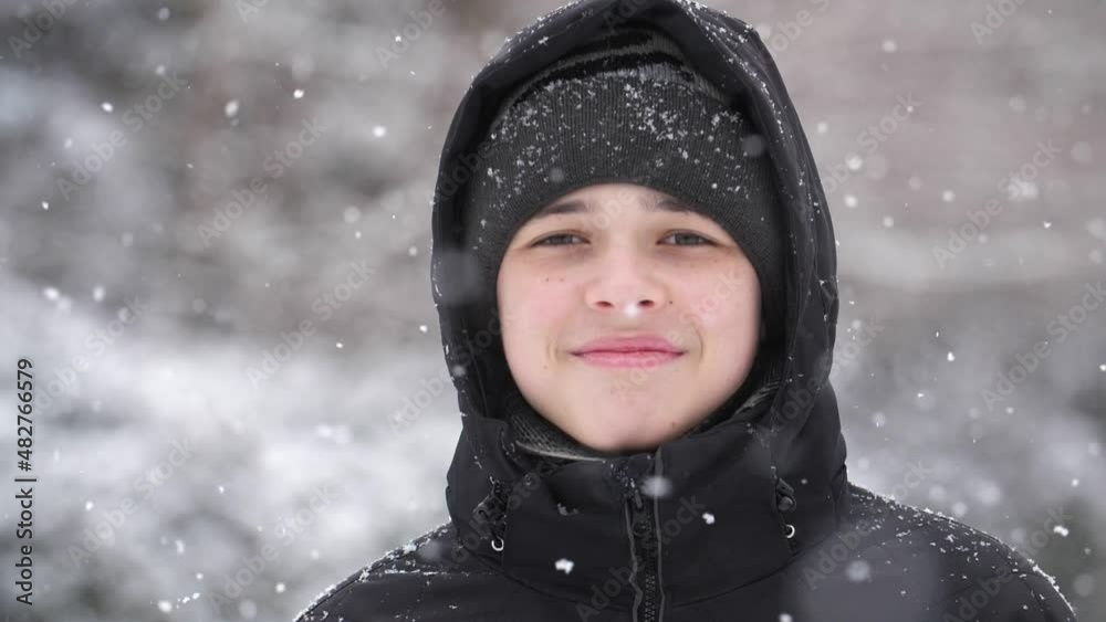 Portrait of a 13-year-old European boy dressed in a black jacket in a heavy snowfall. Slow motion, close-up, shallow depth of field Portrait of a 13-year-old European boy dressed in a black jacket in a heavy snowfall. Slow motion, close-up, shallow depth of field