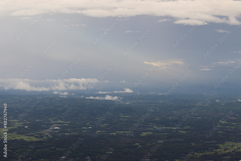 Photos from the viewpoint at the top of Phu Thap Boek, Thailand. Above is a group of cloud and sunlight shines through. below is a forest There are lots of trees, cool weather and strong winds.