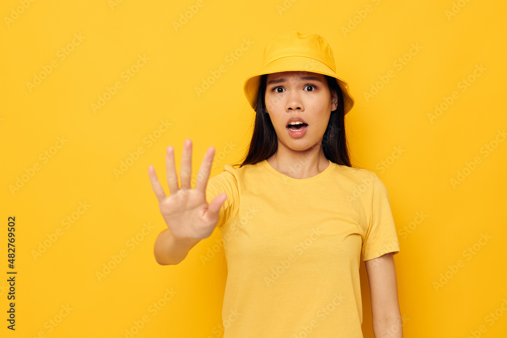 Charming young Asian woman in a yellow t-shirt and hat posing emotions yellow background unaltered
