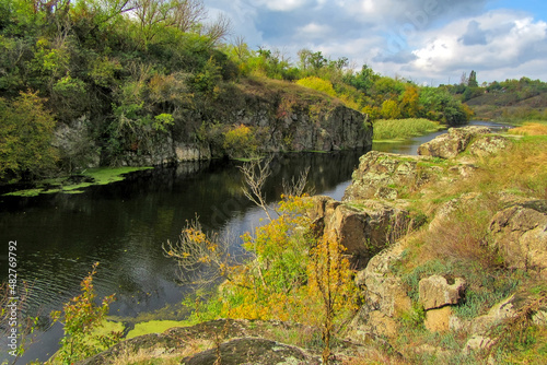 Vertical stone rocks on the bank of the river. A picturesque view of the Tyasminsky canyon with river on sunny day. Kam'yanka Cherkasy region, Ukraine.