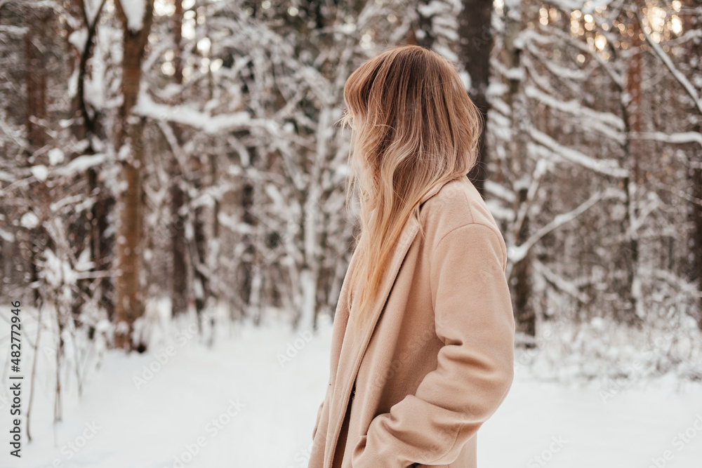 Unrecognizable woman in winter forest looking back. Girl with blonde hair in coat outdoors. Unrecognizable woman in winter forest looking back. Girl with blonde hair in coat outdoors.