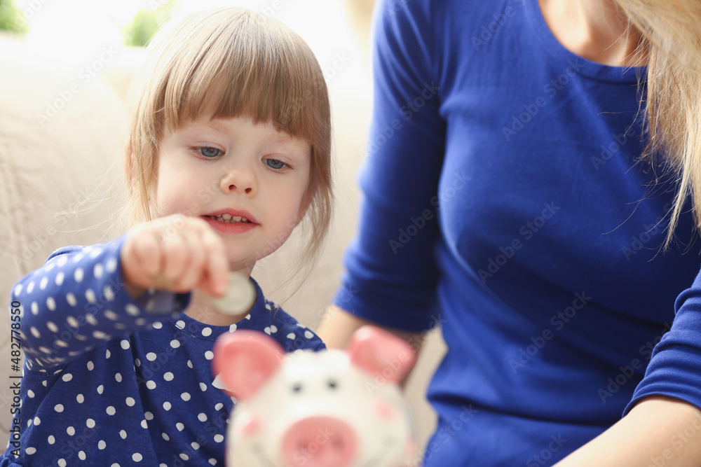 Child little girl putting coin money into piggy bank container Child little girl putting coin money into piggy bank container