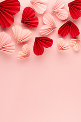 Valentines day, hearts love background for marriage celebration -  beautiful pink, red paper ribbed hearts in origami style fall on pastel pink color as header border, copy space, top view, vertical.