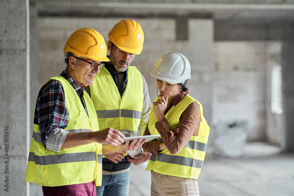 Three caucasian engineers discussing over digital tablet on the construction site Three caucasian engineers discussing over digital tablet on the construction site