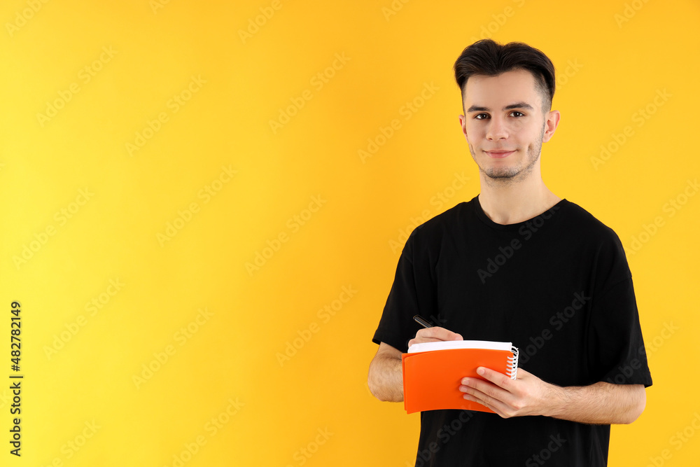 Young man with notebook and pen on yellow background Young man with notebook and pen on yellow background