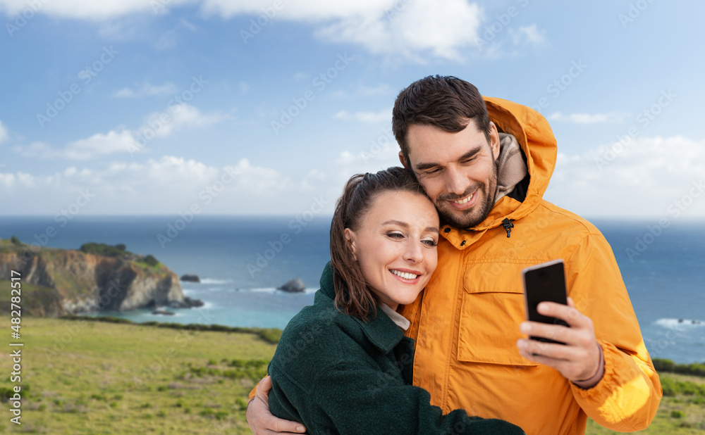 technology, travel and tourism concept - happy couple with smartphone over big sur coast in california background