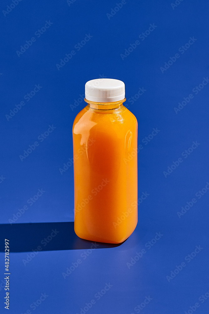 Orange juice bottle on blue background. Drink in plastic bottle. Delivery drink. Trendy mock up bottle concept design. Drink container in minimal style. Orange juice bottle on blue background. Drink in plastic bottle. Delivery drink. Trendy mock up bottle concept design. Drink container in minimal style.