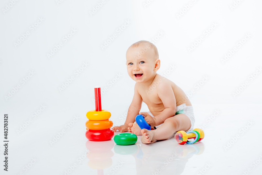 a little baby boy in a diaper is sitting on a white background playing a multi-colored pyramid , studio shooting a little baby boy in a diaper is sitting on a white background playing a multi-colored pyramid , studio shooting